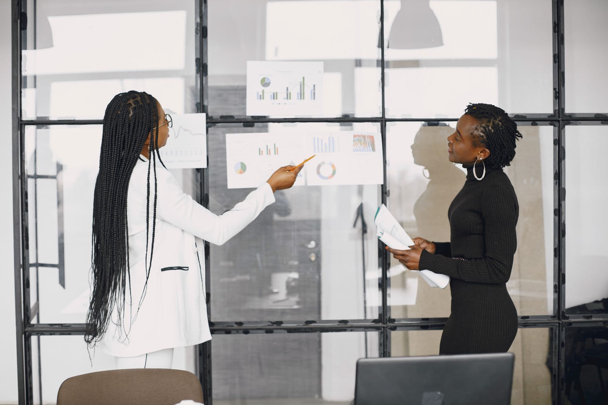 Two businesswomen discussing financial charts on a glass wall